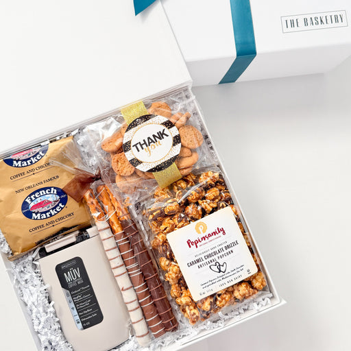 Gift basket with popcorn, pretzels, and a bottle of wine on a white surface with a blue ribbon.