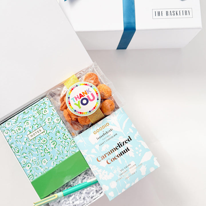Gift set with a notebook, candy, and a box of chocolates in a white box with a blue ribbon.