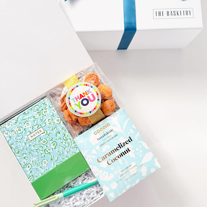 Gift set with a notebook, candy, and a box of chocolates in a white box with a blue ribbon.
