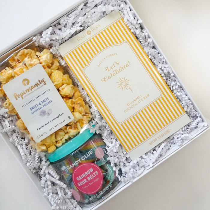 Gift box with popcorn, cookies, and a card on a white surface