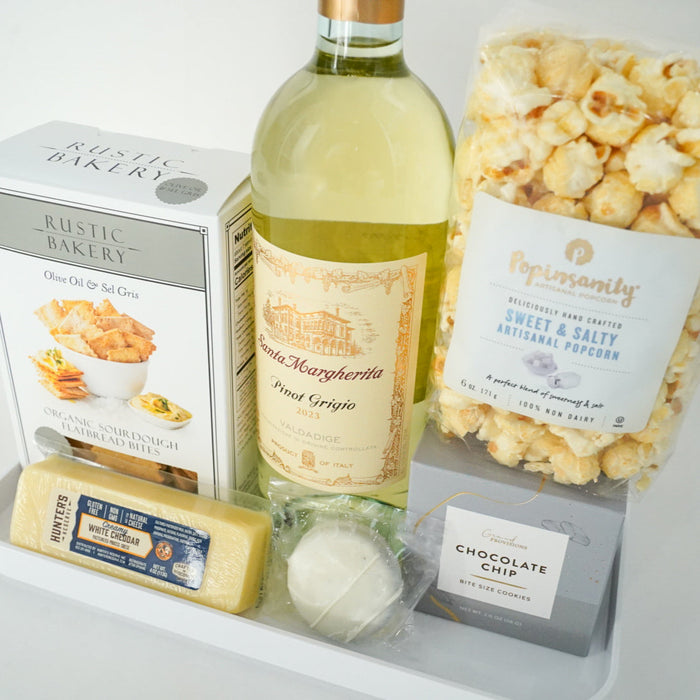 Tray with a bottle of wine, popcorn, cheese, and other snacks on a light background