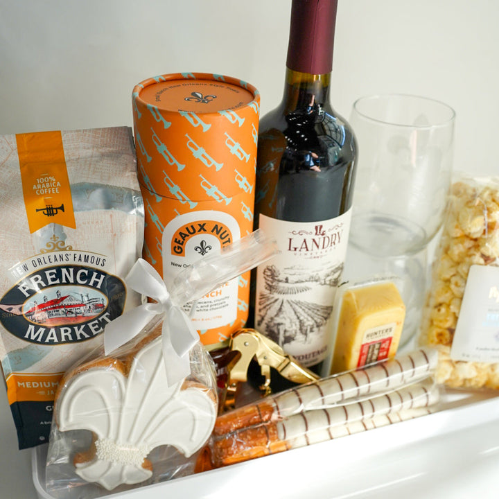 Gourmet gift tray with wine, cheese, and snacks on a white surface