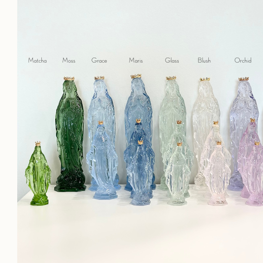 Translucent glass Virgin Mary statues in various colors including Moss green and Orchid purple featuring small gold crowns and available in Tall Medium and Petite sizes on a white surface