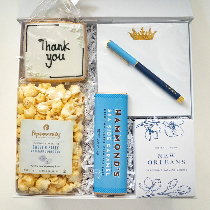 Photograph of a curated gift box featuring a hand-lettered Thank You cookie, a bag of Popinsanity popcorn, a blue Hammond&