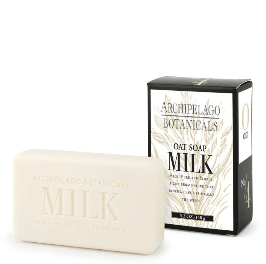 Product photograph by Archipelago Botanicals of an off-white Oat Milk soap bar with embossed lettering and its black and white box featuring golden botanical illustrations on a seamless white background