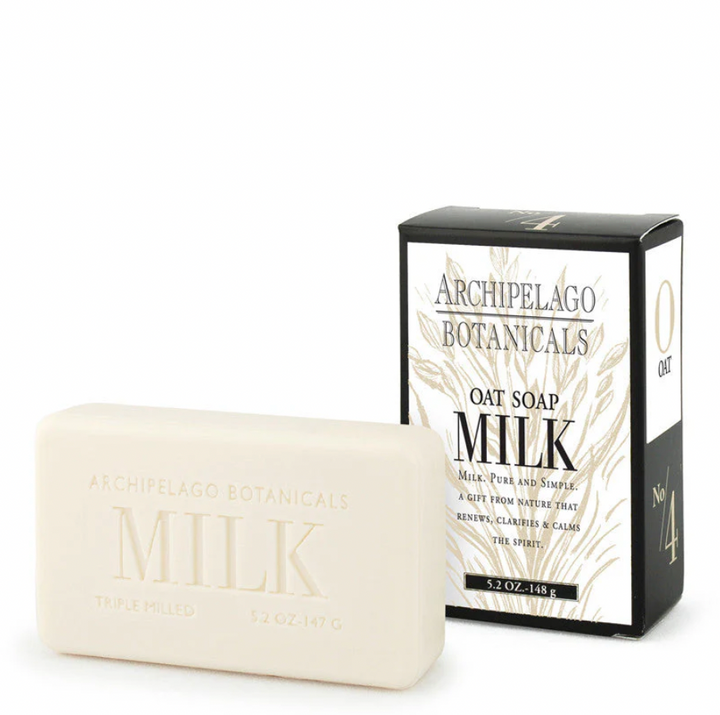 Product photograph by Archipelago Botanicals of an off-white Oat Milk soap bar with embossed lettering and its black and white box featuring golden botanical illustrations on a seamless white background