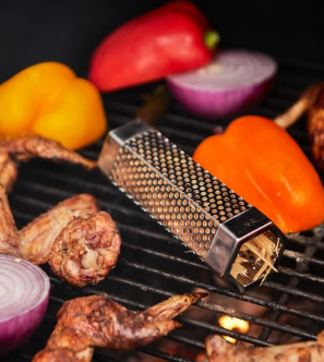 Perforated stainless steel smoker tube on a grill beside chicken wings, bell peppers and red onion