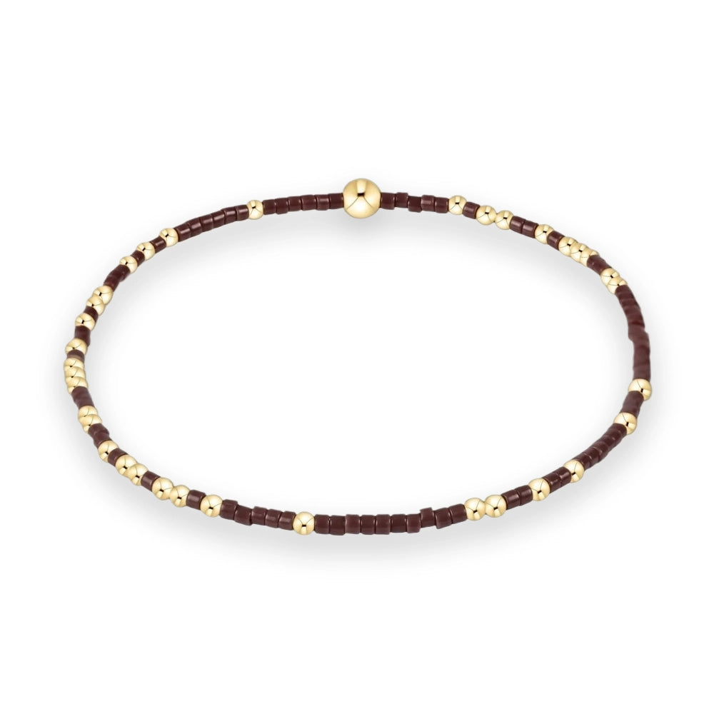 Beaded jewelry handcrafted bracelet on a white background featuring deep maroon cylindrical seed beads interspersed with polished gold spheres and a larger central focal bead
