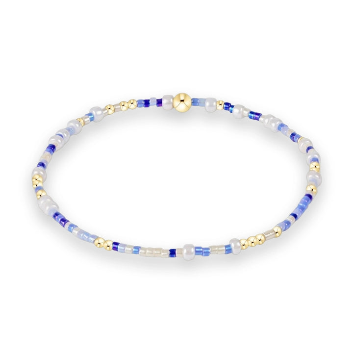Handcrafted beaded bracelet featuring a delicate circular strand of cobalt blue, sky blue, and iridescent white seed beads accented by polished gold spheres on a minimalist white background