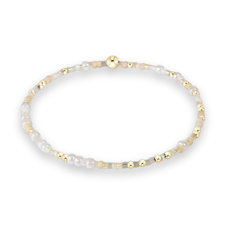 Beaded bracelet featuring a central polished gold bead surrounded by a delicate sequence of pearlescent white, translucent grey, and cream-colored seed beads against a white background