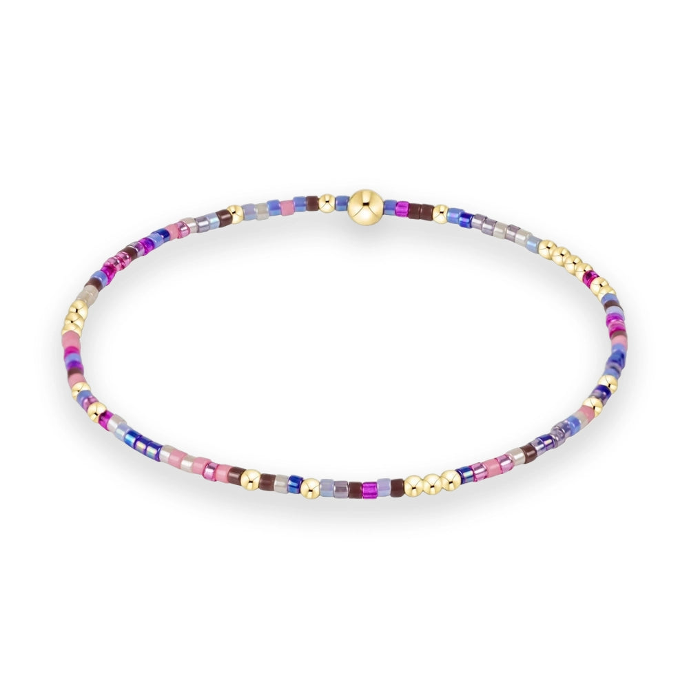 Handcrafted glass and gold bead bracelet showcasing a vibrant pattern of pink, blue, and violet seed beads accented by polished gold spheres and a central gold focal bead on a white background