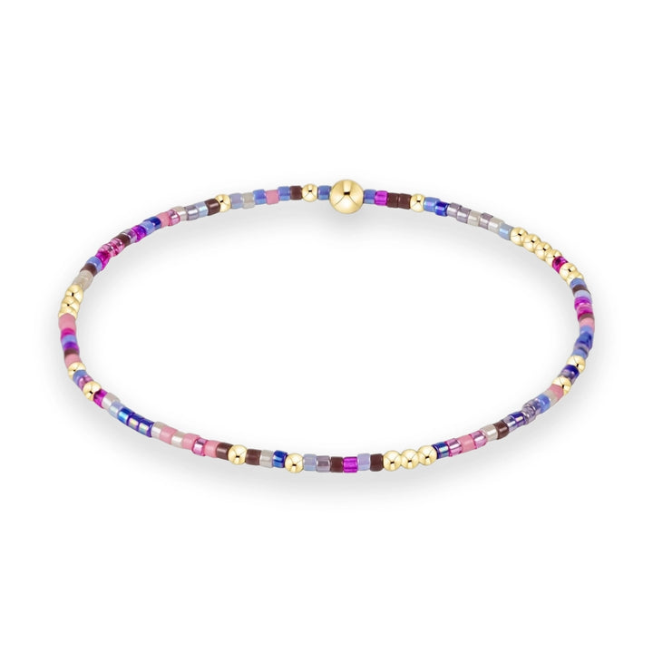 Handcrafted glass and gold bead bracelet showcasing a vibrant pattern of pink, blue, and violet seed beads accented by polished gold spheres and a central gold focal bead on a white background