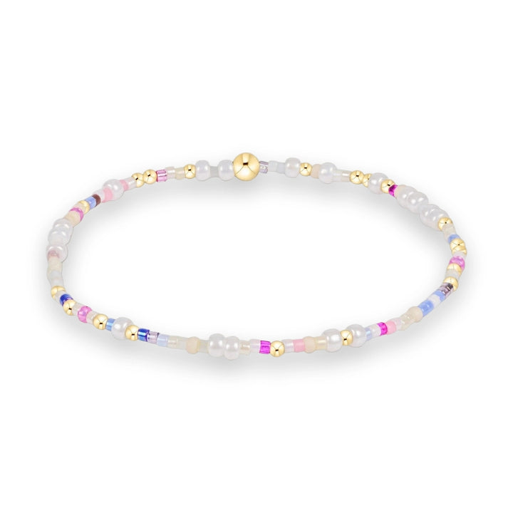 Handcrafted beaded jewelry featuring a colorful seed bead bracelet on a white background with pastel pink and blue accents, interspersed with small gold spheres and iridescent white beads