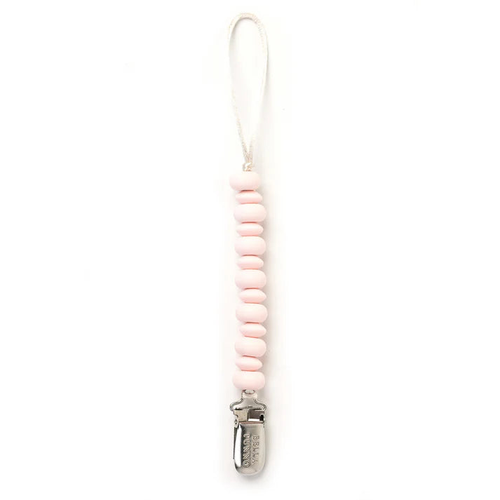 Silicone and metal pacifier clip by Bella Tunno featuring a vertical string of light pink oval beads and a white cord loop terminating in an engraved silver metal clasp against a white background