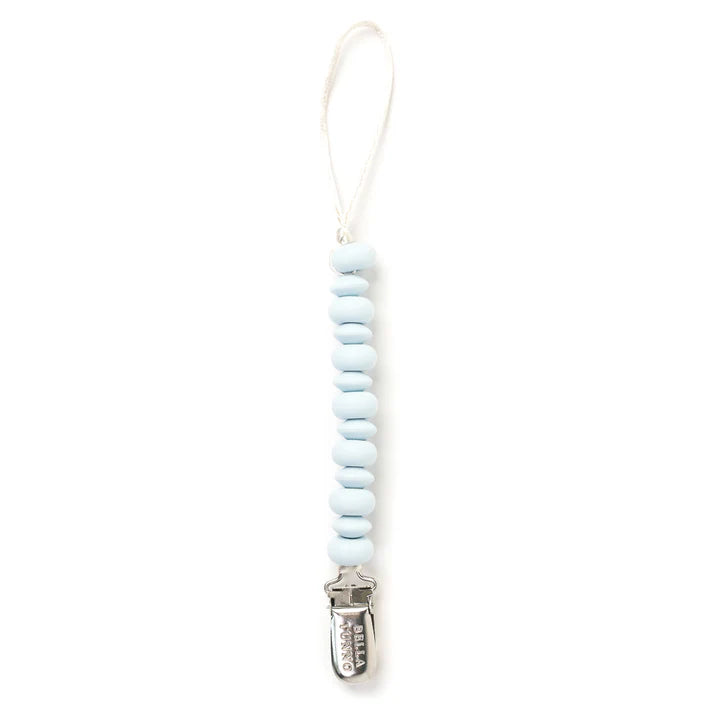 Silicone and stainless steel pacifier clip by Bella Tunno featuring a vertical string of twelve light blue disk-shaped beads with a white cord loop and an engraved silver metal clasp against a white background