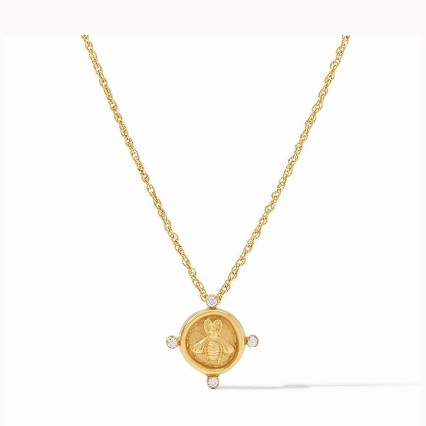 Gold jewelry piece by Julie Vos featuring a honeybee coin pendant centered on a white background with an embossed bee motif, four bezel-set clear crystals at the cardinal points, and a delicate gold rope chain