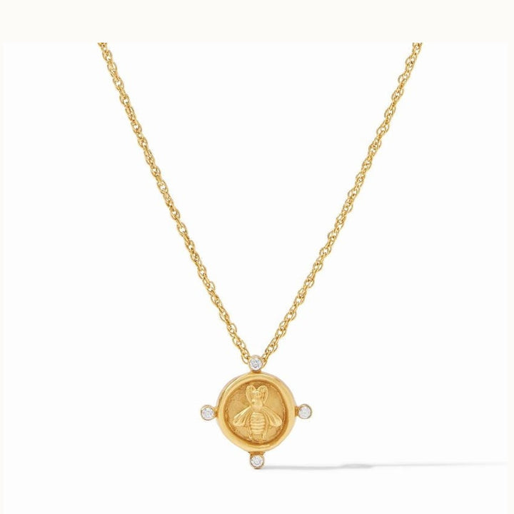 Gold jewelry piece by Julie Vos featuring a honeybee coin pendant centered on a white background with an embossed bee motif, four bezel-set clear crystals at the cardinal points, and a delicate gold rope chain
