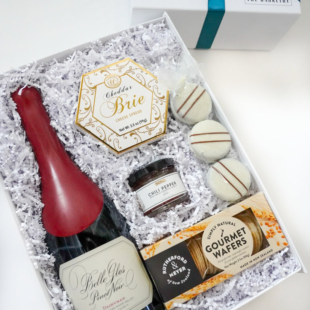 Gift set with a bottle of wine, cookies, and other treats in a decorative box.