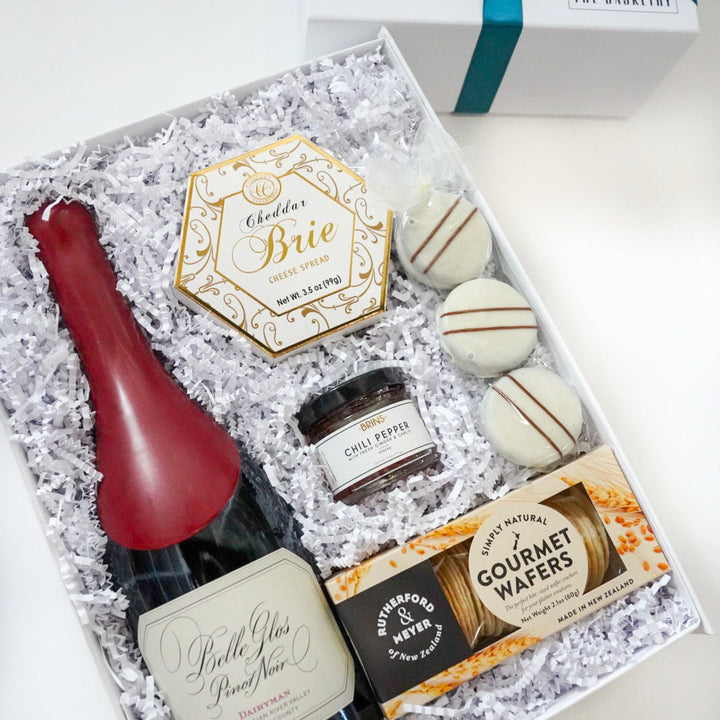 Gift set with a bottle of wine, cookies, and other treats in a decorative box.
