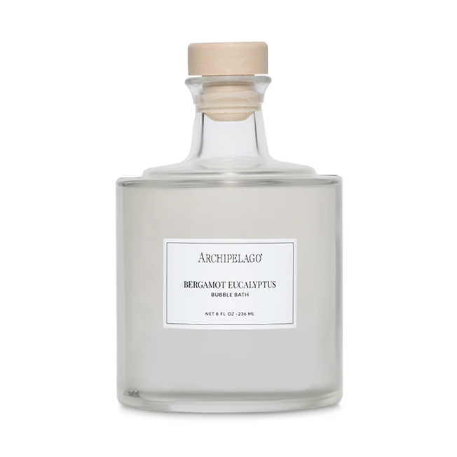 Product photography by Archipelago of a Bergamot Eucalyptus Bubble Bath bottle on a white background featuring a clear square-shouldered glass vessel, a natural wooden cork stopper, and a minimalist white label with black serif text