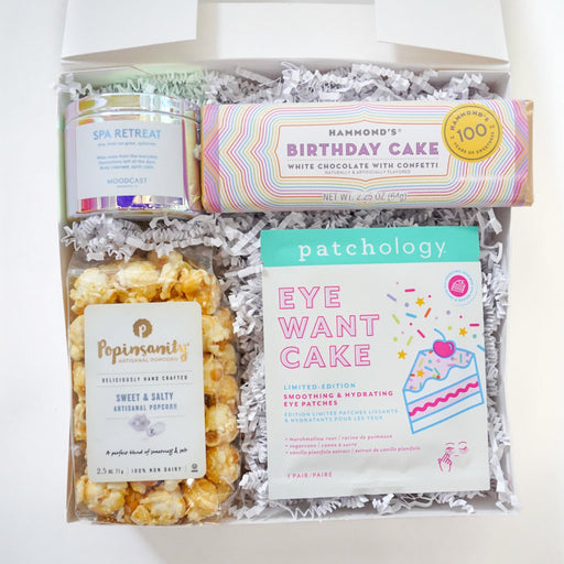 Gift basket with various items including popcorn, candy, and eye care products on a white background