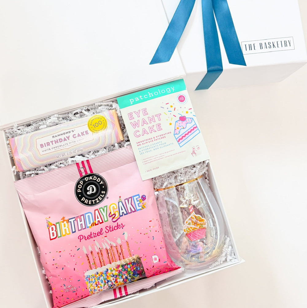 Gift set with pink packaging, blue ribbon, and birthday-themed items on a white background