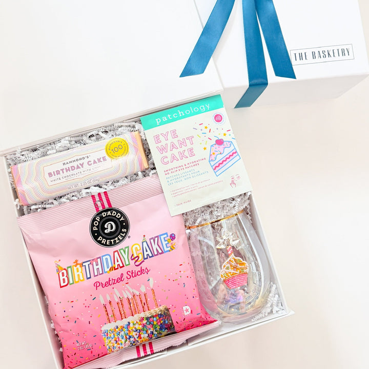 Gift set with pink packaging, blue ribbon, and birthday-themed items on a white background