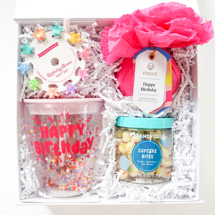 Gift box with birthday-themed items including a tumbler, cookies, and a pink flower on a white background.