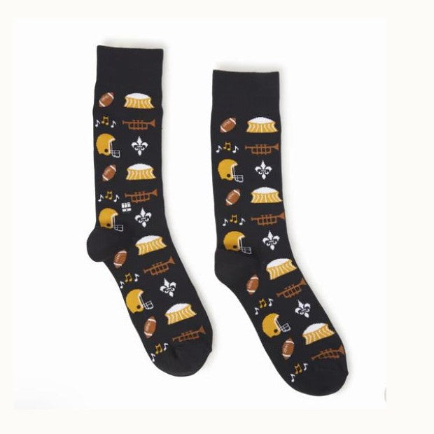 Knitted black crew socks featuring a New Orleans sports theme with repeating patterns of the Caesars Superdome, gold football helmets, and white fleur-de-lis symbols alongside orange trumpets