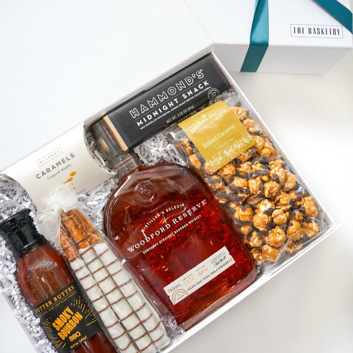 Gift set with a bottle of whiskey, snacks, and a bottle of hot sauce on a white surface.
