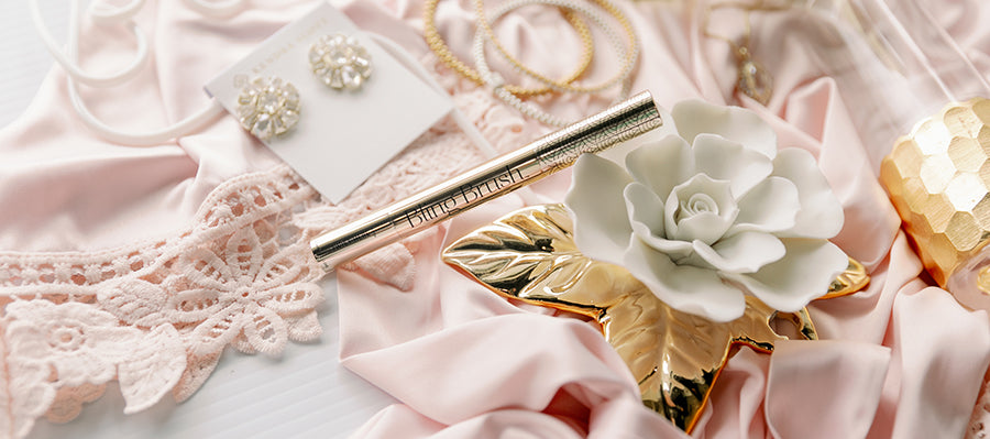 Bridal gift photo featuring Kendra Scott earrings, a Bling Brush jewelry cleaner, a gold bottomed champagne flute, and a ceramic gold flower to mount on the wall.