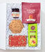 An open white gift box filled with shredded white paper and containing assorted gourmet snacks and treats, including a red bag labeled Fortune Favors, a small jar, a hexagonal box labeled Brie, a red chocolate bar, and a green bag of 345 Crisps, photographed on a light neutral background.