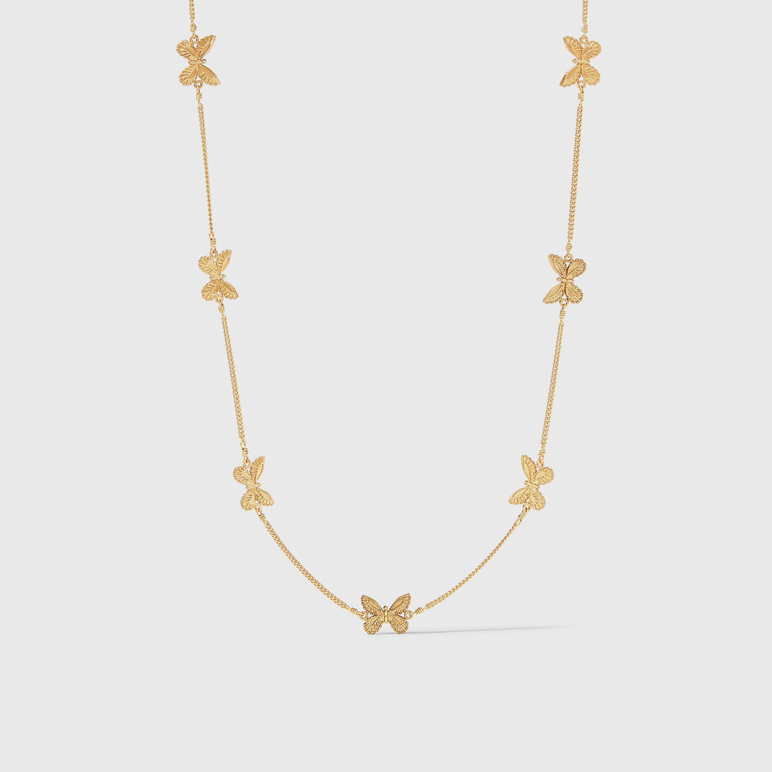 Gold butterfly necklace featuring seven finely textured insect charms spaced symmetrically along a delicate gold chain against a minimal grey background