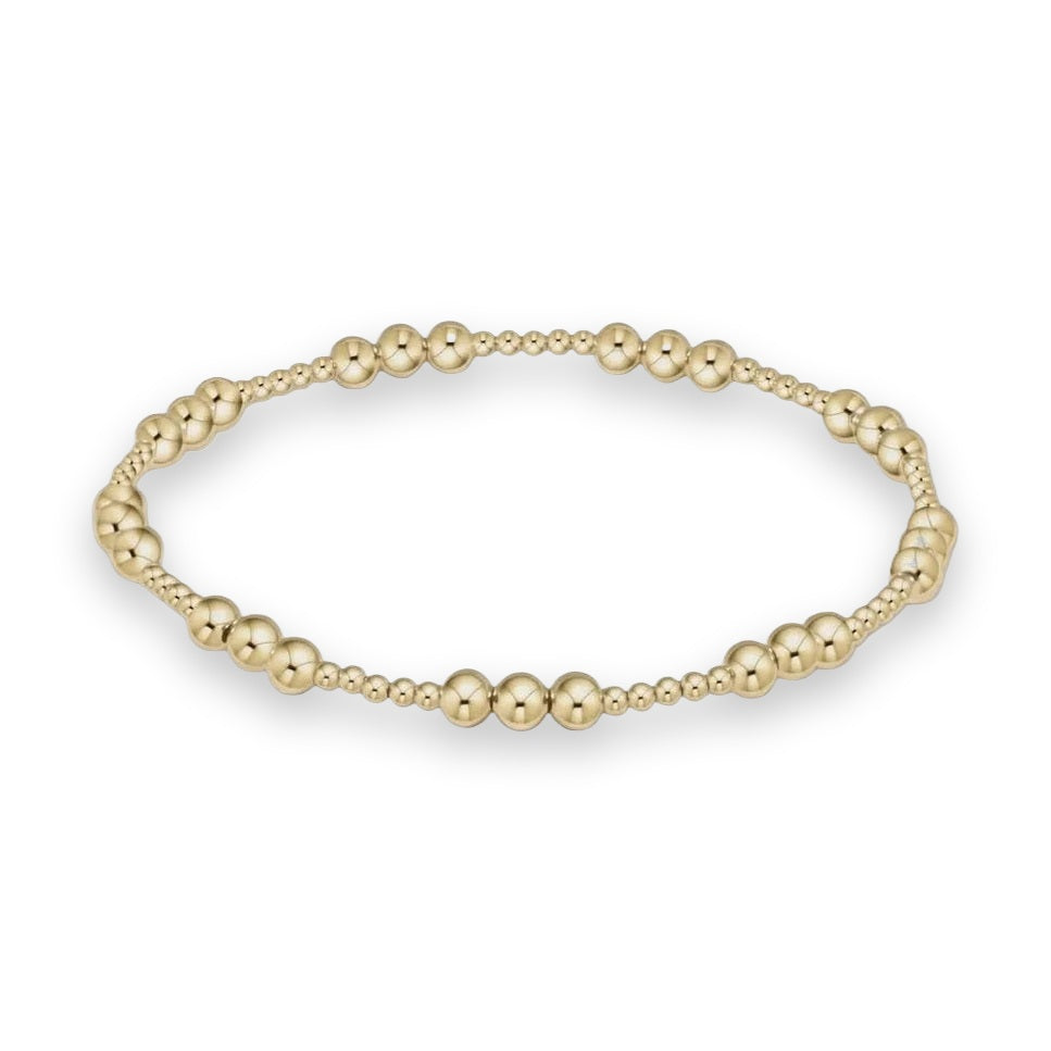 Polished yellow gold beaded bracelet featuring a rhythmic pattern of varying spherical bead sizes and a high-shine reflective finish arranged in a seamless circle on an off-white studio background