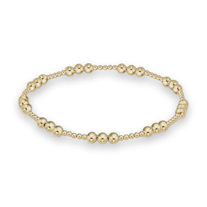 Polished yellow gold beaded bracelet featuring a rhythmic pattern of varying spherical bead sizes and a high-shine reflective finish arranged in a seamless circle on an off-white studio background