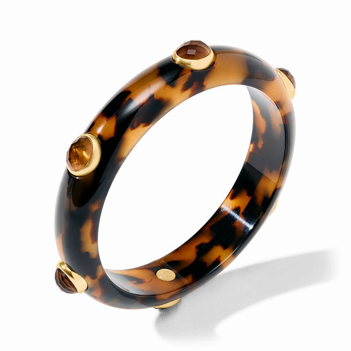 Tortoiseshell resin bangle by Seaman Schepps featuring faceted brown gemstones in gold-tone bezel settings against a white studio background with unique mottled patterns and a polished finish