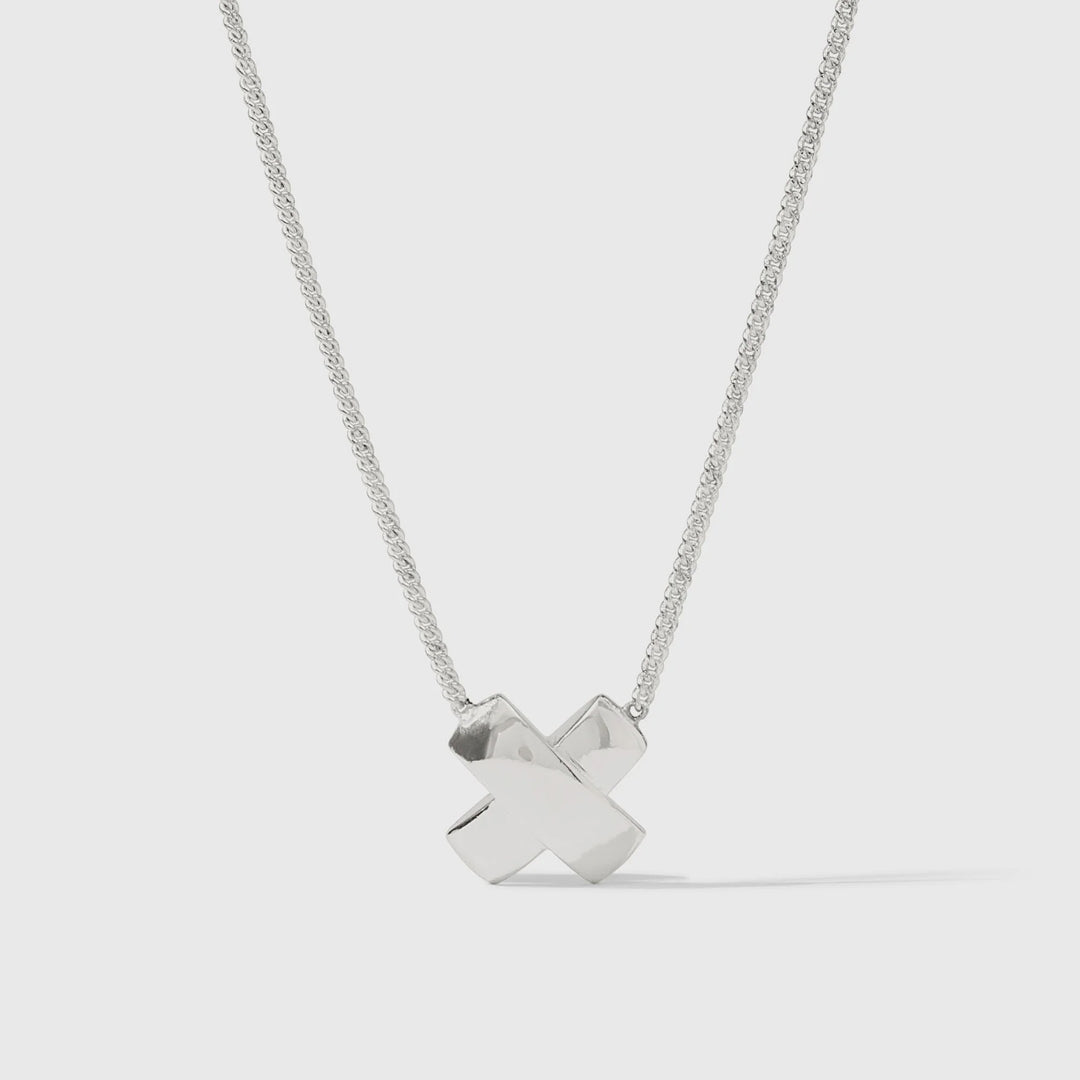Sterling silver necklace by Paloma Picasso featuring a polished X-shaped kiss pendant on a delicate curb chain in a neutral studio setting with reflective highlights and a soft shadow