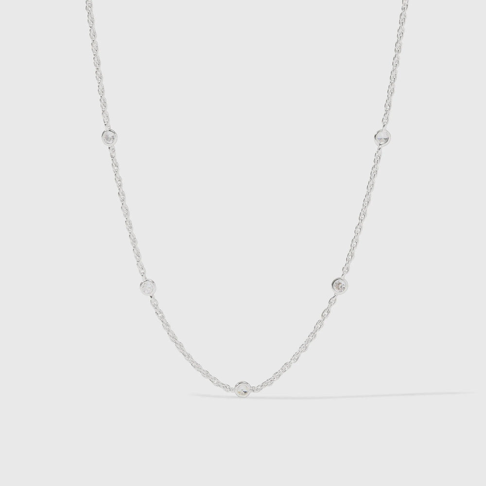 Sterling silver jewelry necklace featuring a delicate cable chain with five circular bezel-set clear crystals and a polished metallic finish against a light gray studio background