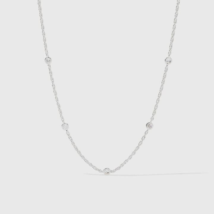 Sterling silver jewelry necklace featuring a delicate cable chain with five circular bezel-set clear crystals and a polished metallic finish against a light gray studio background