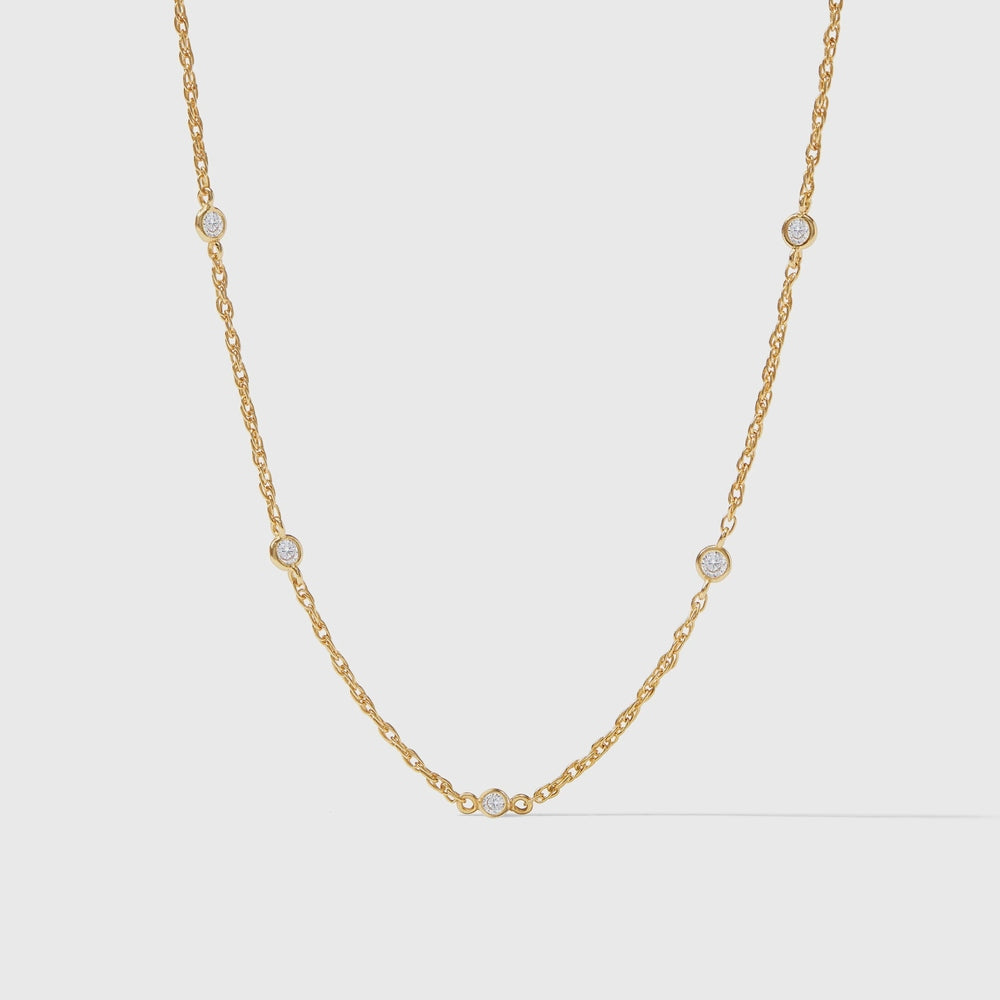 Yellow gold and diamond station necklace featuring five round bezel-set stones on a delicate twisted rope chain against a neutral light gray studio background
