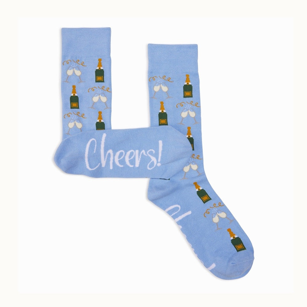 Product photograph of light blue crew socks on a white background featuring a repeating pattern of green champagne bottles with gold labels and clinking glasses with white bubbles alongside the word Cheers in white script on the sole