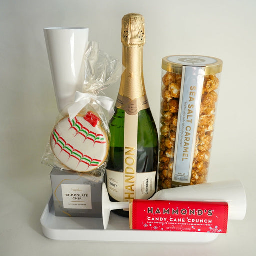 Gift set with champagne, cookies, and snacks on a white surface