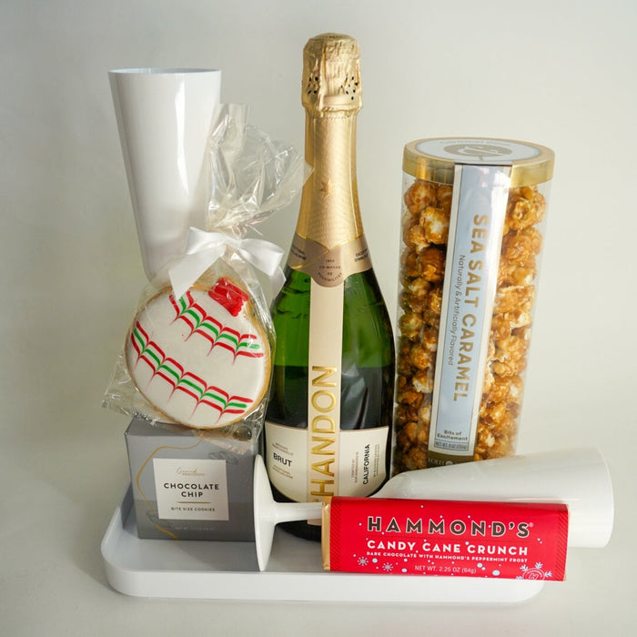 Gift set with champagne, cookies, and snacks on a white surface