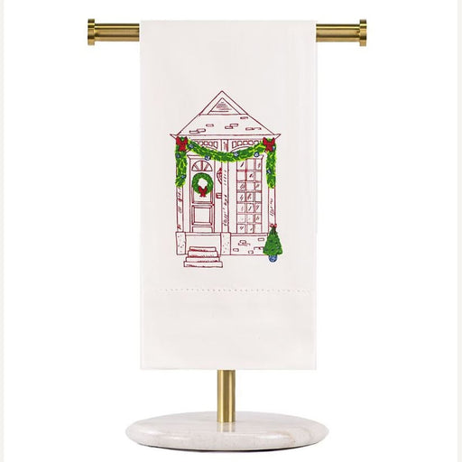 Embroidered linen hand towel by Hibiscus Linens featuring a festive boutique storefront entrance adorned with green garlands, a red-bowed wreath, and a small potted Christmas tree displayed on a gold and marble stand