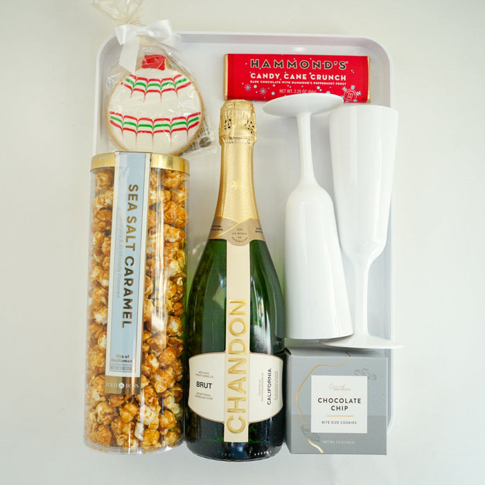 Bottle of champagne with a bag of sea salt caramel popcorn and a box of chocolate crisps on a white surface.