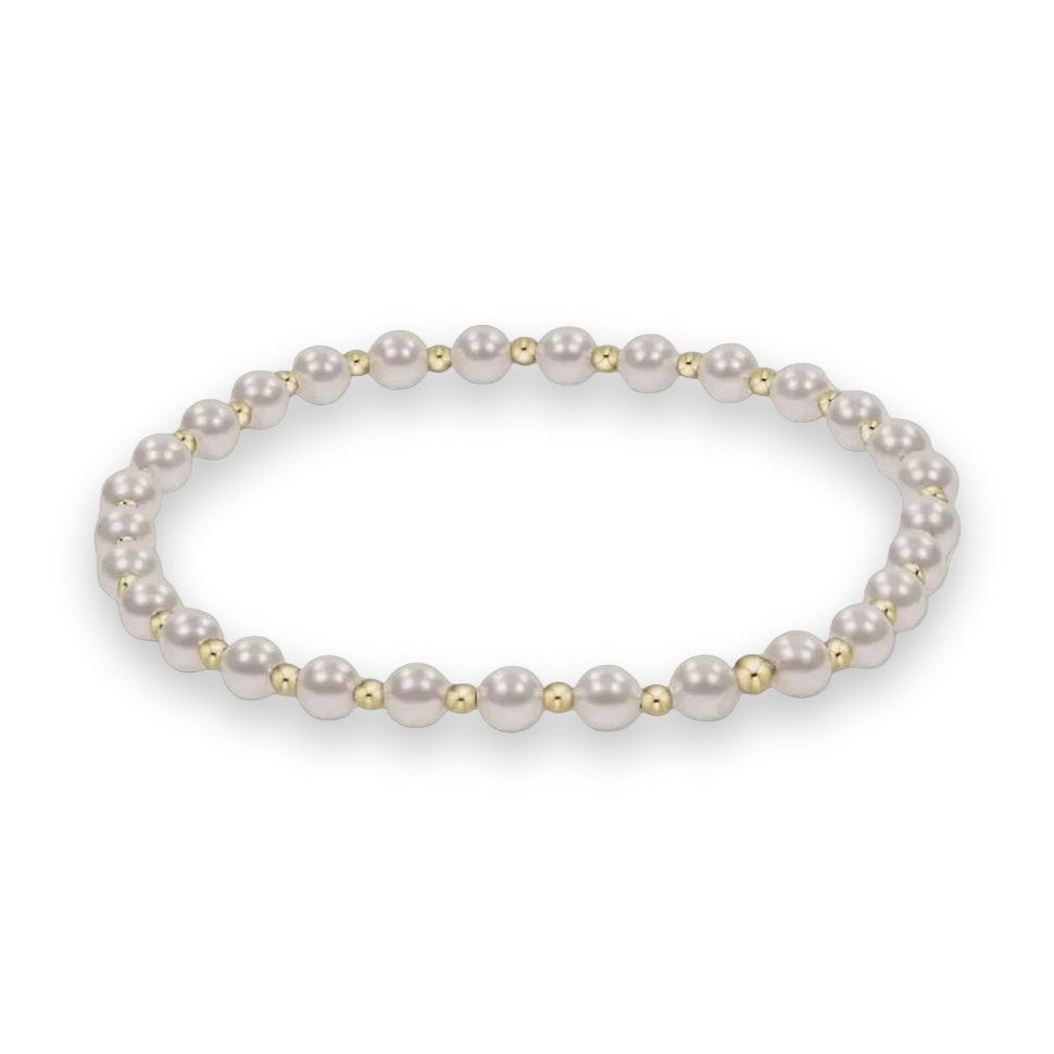 Fine jewelry photograph of a pearl and gold bead stretch bracelet centered on a neutral background featuring an alternating sequence of lustrous white pearls and polished yellow gold spacer beads