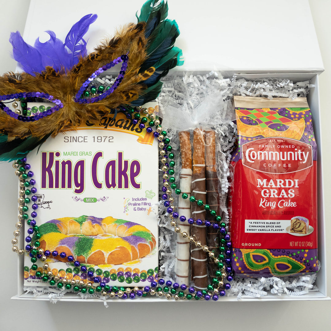 Photograph of a New Orleans Mardi Gras gift box containing Mam Papaul's King Cake mix, Community Coffee, chocolate-drizzled pretzel rods, a purple feathered sequin mask, and strands of metallic beads