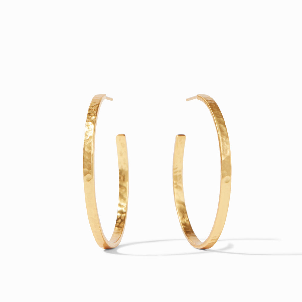 Hammered gold jewelry by Julie Vos featuring a pair of large open hoop earrings on a minimalist white background with a glistening dimpled texture and a warm light-reflecting finish