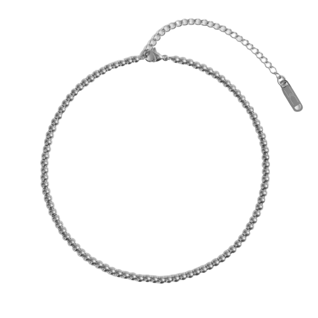 Polished silver jewelry product photograph of a beaded ball necklace on a minimalist white background featuring a secure lobster clasp, a linked extender chain, and a rectangular metal logo charm