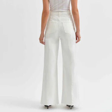Studio photograph of a model from the rear wearing white high-waisted wide-leg denim jeans featuring vertical seam panels and frayed raw hems in a bright studio setting